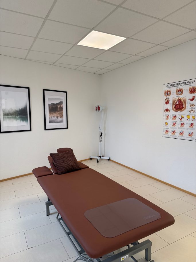 Ein Behandlungsraum mit einer Liege und medizinischer Wandgrafik.