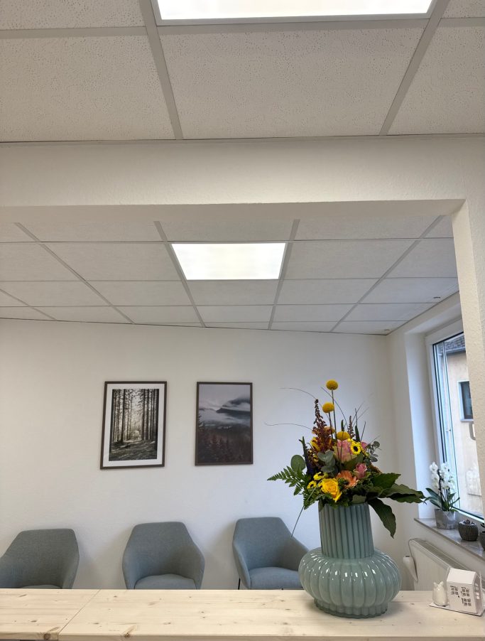 Heller Empfangsbereich mit Blumenschmuck und zwei Bildern an der Wand.