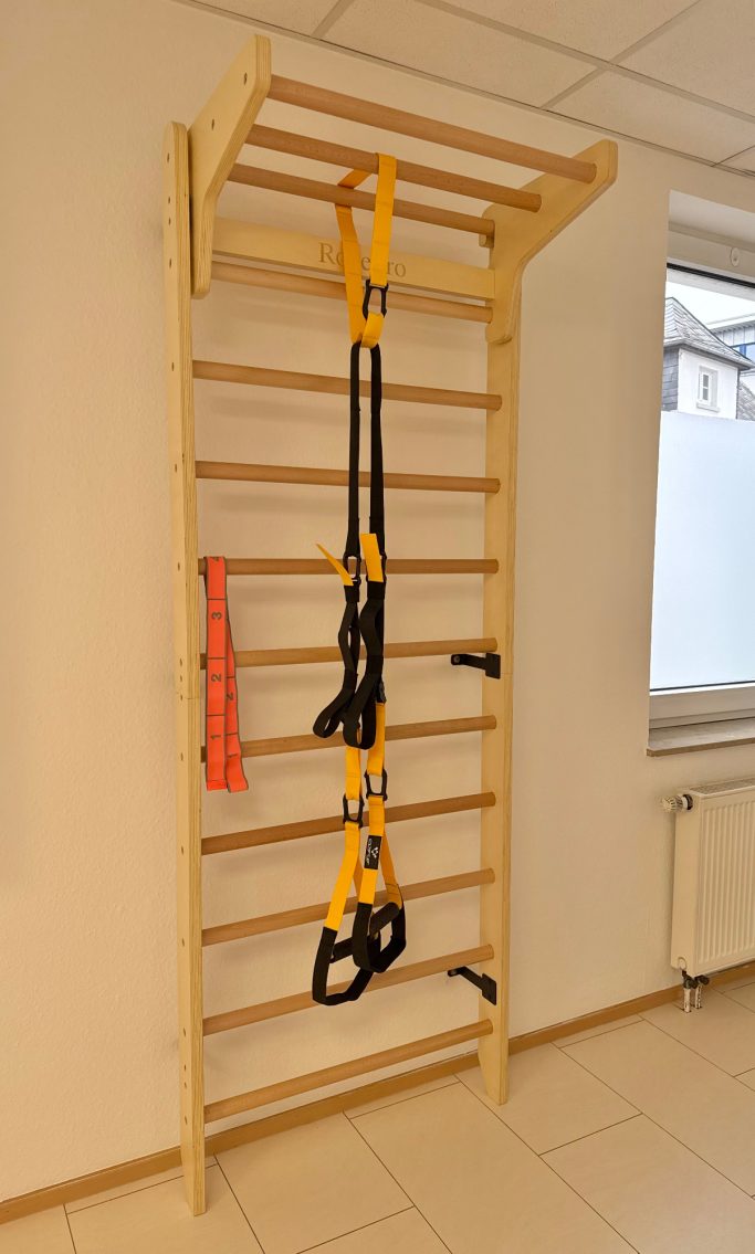 Holz-Kletterwand mit gelben TRX-Trainingselementen und orangefarbener Sicherungsleine.
